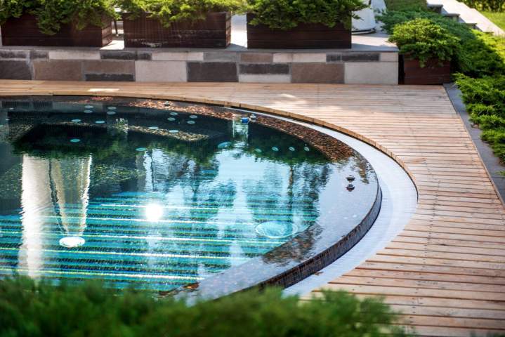 Aménagement extérieur autour dune piscine avec terrasse en bois et végétation méditerranéenne, créant une ambiance de vacances.